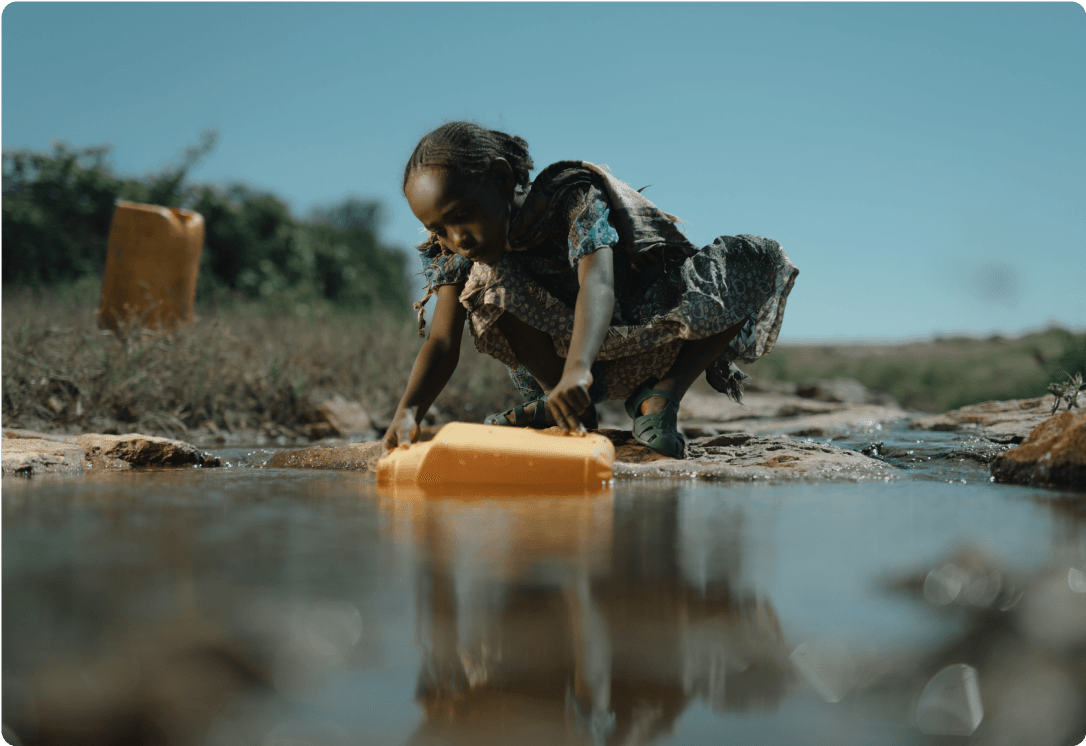 Girl filling jerry can with water from a pond.